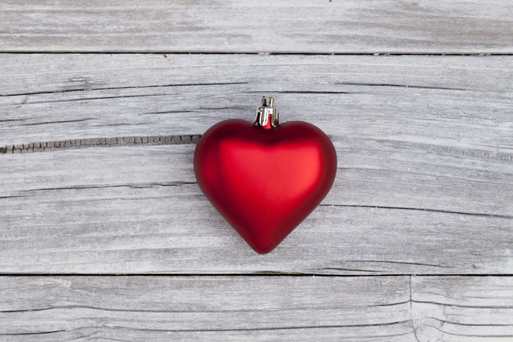 Immagine di una decorazione a forma di cuore rosso brillante su una superficie di legno grigia, perfetta per rappresentare il tema di San Valentino esperienze, evocando romanticismo e semplicità.