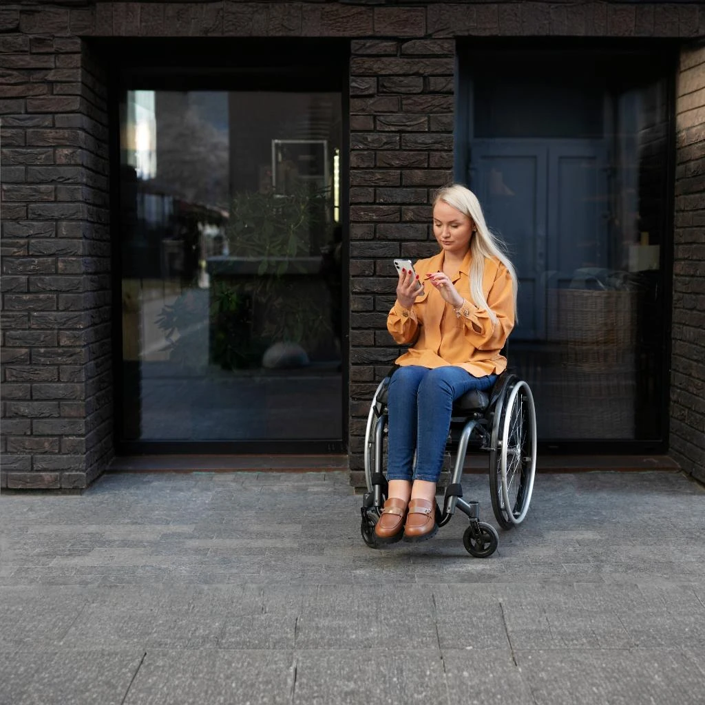 Una donna in sedia a rotelle utilizza il suo smartphone per esplorare un sito di accessibilità e-commerce, dimostrando inclusività digitale.